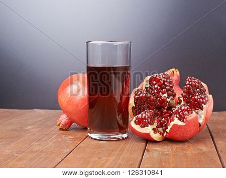 Pomegranate Punica granatum fruit next to the tall glass full of red juice, composition placed over the wooden boards surface