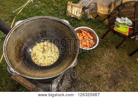 Large Old Fashioned Iron Kettle and Onion Grilling Bowl with Carrot and other Ingredients and Kitchen Utensils on Background