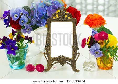 Colorful violets and pancies cut flowers in vases, copy space on empty antique frame