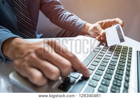 Man holding credit card in hand and entering security code using smart phone on laptop keyboard online shopping concept.