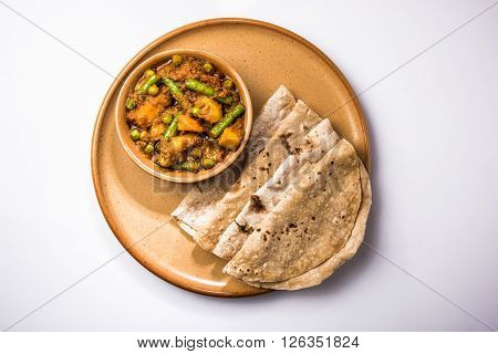 indian recipe, mixed veg containing potato and beans with traditional masala and curry, red hot and spicy served with traditional chapati / fulka / indian roti / indian bread in ceramic plate isolated