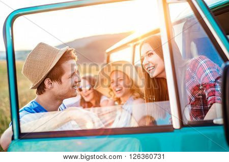 Group of teenage hipsters on a roadtrip having fun, standing at the campervan. Young friends outside on a summer day.