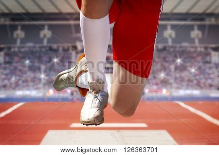 Long jumper in a stadium jumps into the sand box. The background shows fully occupied spectator terraces with sparkling flashlights.
