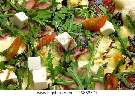 Appetizing pizza with ham, salami, arugula, cherry tomatoes, fetaksa, balsamic closeup