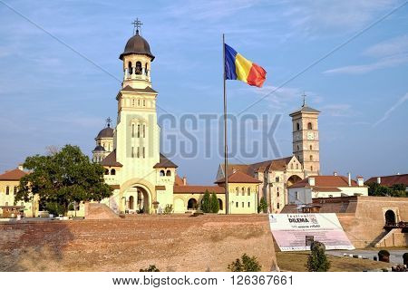 ALBA IULIA, ROMANIA - AUGUST 11, 2015: the Romanian flag waving between the Orthodox Coronation Cathedral  and St. Michael Roman Catholic Cathedral in Carolina Citadel of Alba Iulia