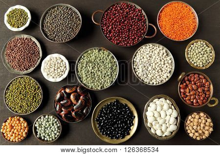 Beans peas and lentils in metal bowls on dark background.