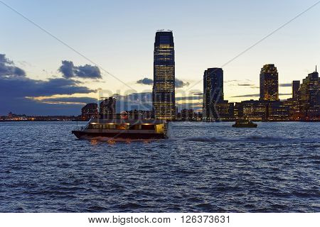 View from Esplanade of Lower Manhattan New York USA on Ferry and skylines in Paulus Hook Jersey City New Jersey USA. Skyscrapers illuminated in the evening. Hudson River