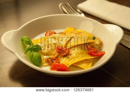 Top-shot of Ravioli with tomatoes and basil in a white dish