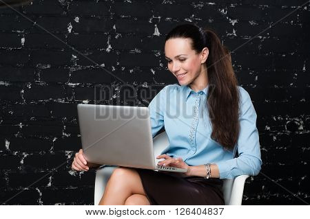 Russian business lady looking to the laptop on the black brick background for use e.g. in collages, presentation