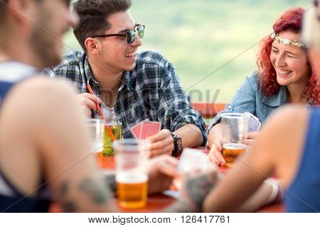 Curly ginger girl and guy make jokes and laugh with friends while playing cards and drinks beer