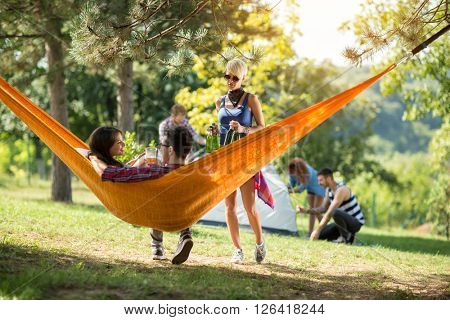 Friend from camp brings beer bootless for couple in love in hammock in nature