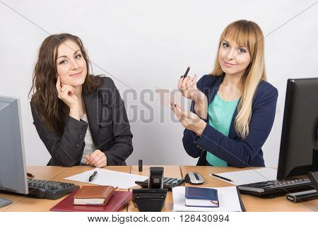 Office Employee Watches As A Colleague Is Going To Make Up Lips At The Desk