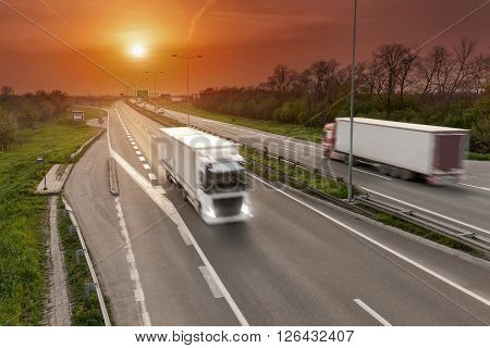 Two trucks driving towards the sun in blurred motion on the freeway at beautiful sunset. Transport scene on the motorway near Belgrade Serbia.