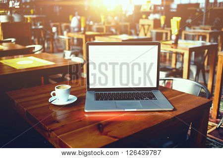 Open laptop computer and cup of coffee lying on a wooden table in cafe bar interior portable net-book with copy space screen for your information content or text message distance work via internet