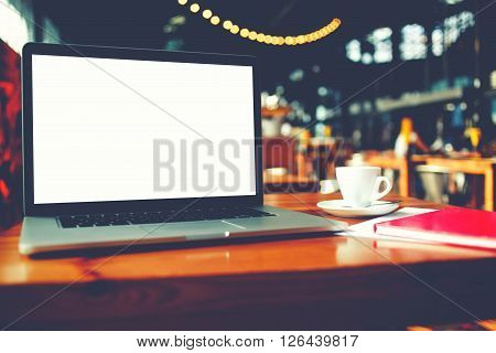 Portable laptop computer with blank copy space screen for text message or promotional content net-book and notepad lying on table in cafe bar interior distance work via internet during coffee break