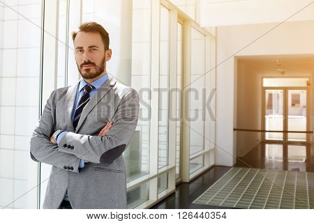 Successful businessman dressed in expensive suit is standing in hallway his company near copy space for your advertising text message or promotional content.Young male manager is posing after briefing