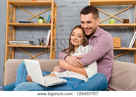 Happy Couple In Love Sitting On The Sofa With Laptop And Doing Shopping