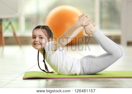Little cute girl practicing yoga pose on a mat indoor