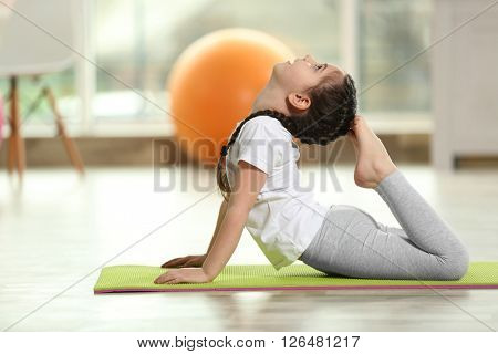 Little cute girl practicing yoga pose on a mat indoor