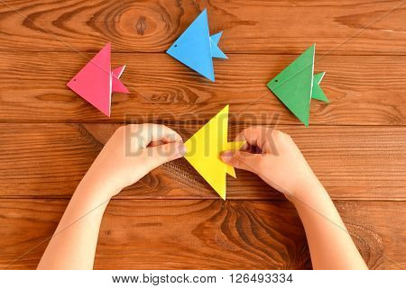 Origami colorful fish. Child holds an yellow origami fish in his hands. Brown wooden background