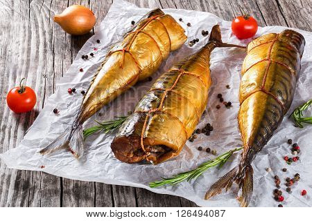 Smoked fish Mackerel or Scomber on a white parchment paper with cherry tomatoes rosemary and spices on an old wooden table studio lights top view