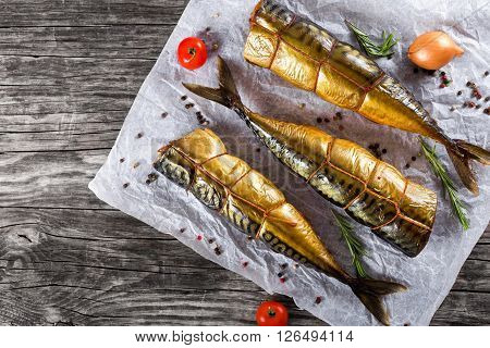 Smoked fish Mackerel or Scomber on a white parchment paper with cherry tomatoes rosemary and spices on an old wooden table studio lights top view