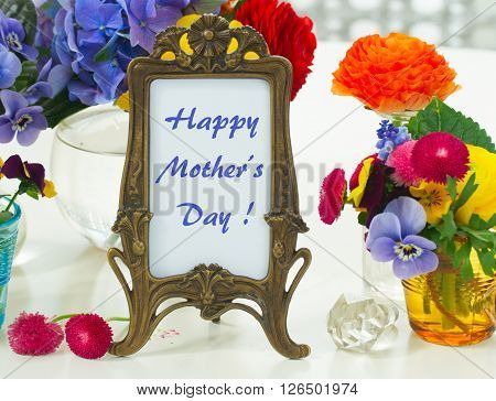 Colorful violets and pancies cut flowers in vases, happy mothers day greeting in antique frame
