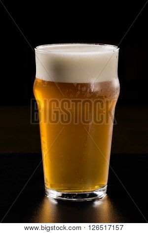 Glass of beer with foam on black background.