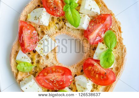 Italian starter friselle. Classical frisella tomato, cheese mozzarella and basil with oregano and olive oil. Dried bread called freselle on white plate. Italian food. Healthy vegetarian food.