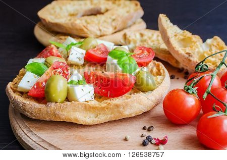 Italian appetizer Friselle. Italian dried bread Friselle on wooden board with tomatoes cherry, basil and pepper. Italian food. Healthy vegetarian food. Selective focus.