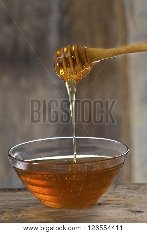 Honey pouring from drizzler into the bowl on wooden table