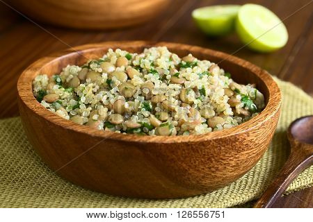 Quinoa salad with lentils and parsley in wooden bowl photographed on dark wood with natural light (Selective Focus Focus one third into the salad)