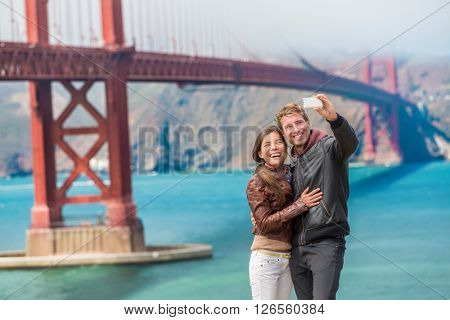 Happy young couple tourists taking selfie in San Francisco by Golden Gate Bridge, USA. Interracial young modern couple using smart phone. Asian woman, Caucasian man.