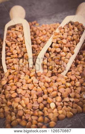 Vintage photo Heap of uncooked brown buckwheat groats with wooden spoon lying on structure of concrete concept for healthy eating and nutrition