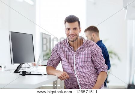 business, technology, education and people concept - happy young creative man or student with computer at office