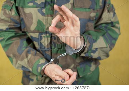 Young man in handcuffs wearing camouflage uniform in the room.
