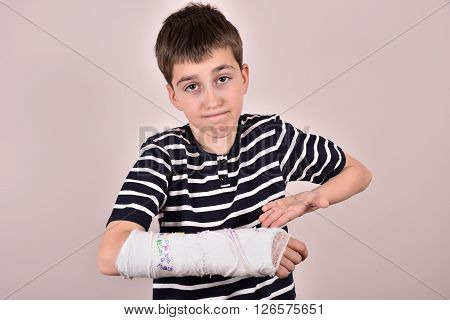 Young boy making a grimace and showing his broken arm with plaster that has been autographed by friends