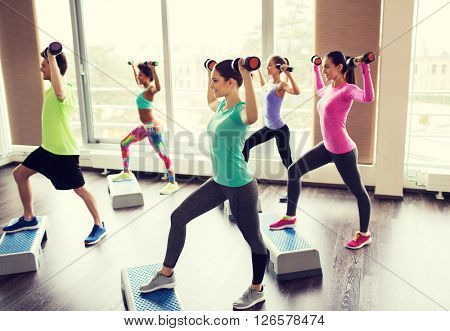 fitness, sport, aerobics and people concept - group of smiling people working out with dumbbells flexing muscles on step platforms in gym
