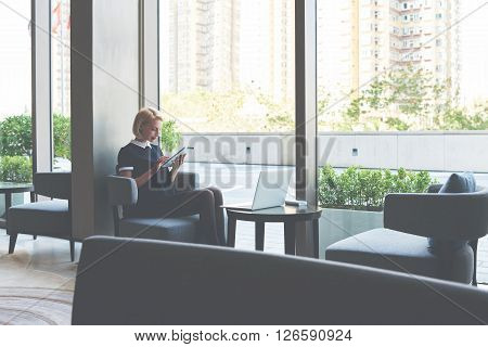 Female student is checking e-mail on digital tablet while is waiting file download on laptop computer. Businesswoman is ordering on-line car via touch pad while is sitting with net-book in cafe