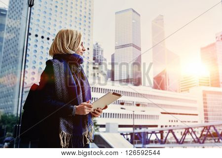 Young hipster girl is holding digital tablet and looking in window at active life of big metropolitan city with tall skyscrapersbackground with copy space for your advertising text message or content