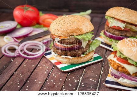Closeup of home made burgers on sesame buns with beef patties and fresh salad ingredients on wooden background