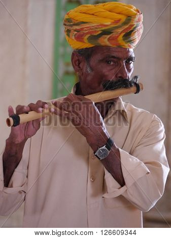 RAJASTHAN, INDIA: MARCH 2016 Close up of a Rajasthani man with the colourful turban and large moustache, typical of that northwestern state of India, playing a traditional wooden flute.
