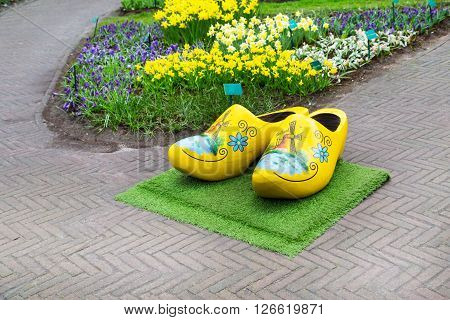 Typical yellow dutch wooden clogs or klompen, painted with windmill and flowerbed behind