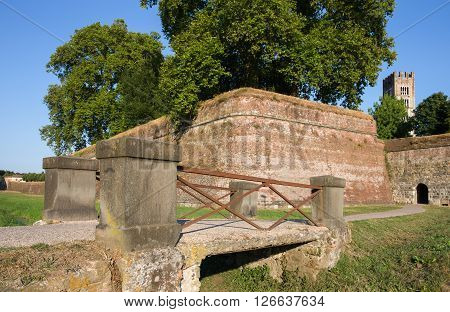 Medieval wall surrounding the Tuscan village of Lucca Italy. Low angle view with a walking bridge in the foreground. The wall was built between 1545 and 1550. It currently serves as a pedestrian walkway and tourist attraction.