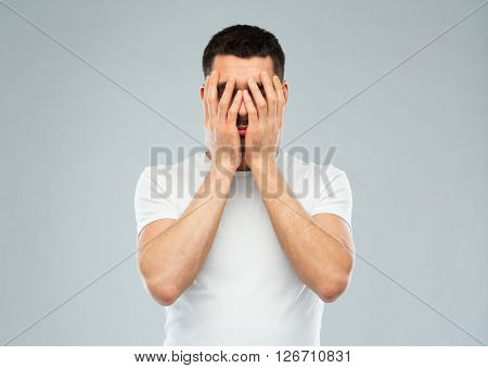 people, crisis, emotions and stress concept - man in white t-shirt covering his face with hands over gray background