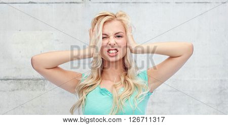 emotions, expressions, stress and people concept - young woman holding to her head and screaming over gray concrete wall background