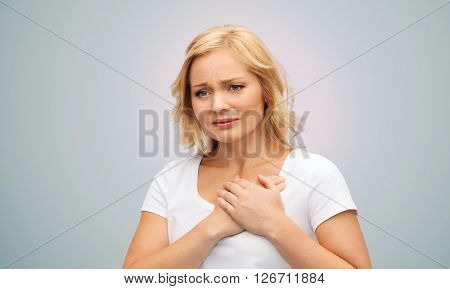 people, healthcare, heart disease and problem concept - unhappy woman suffering from heartache over gray background