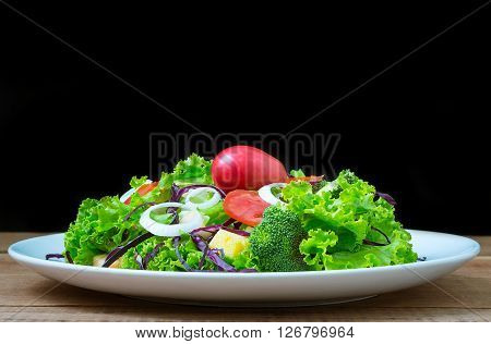 Plate of green salad with vegetables on wooden table.