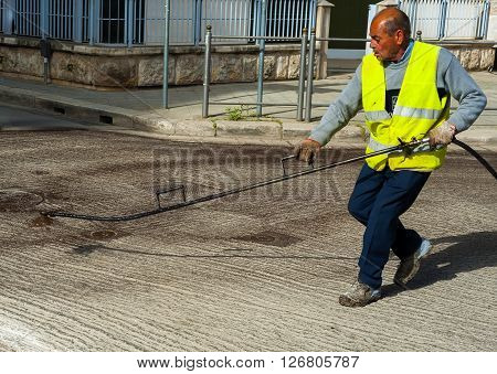 Road worker spraying bitumen emulsion with the hand spray lance before applying a new layer of asphalt