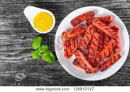 Grilled sausages decorated with basil leaves on a white dish on an old rustic table mustard in a gravy boat studio lights top view